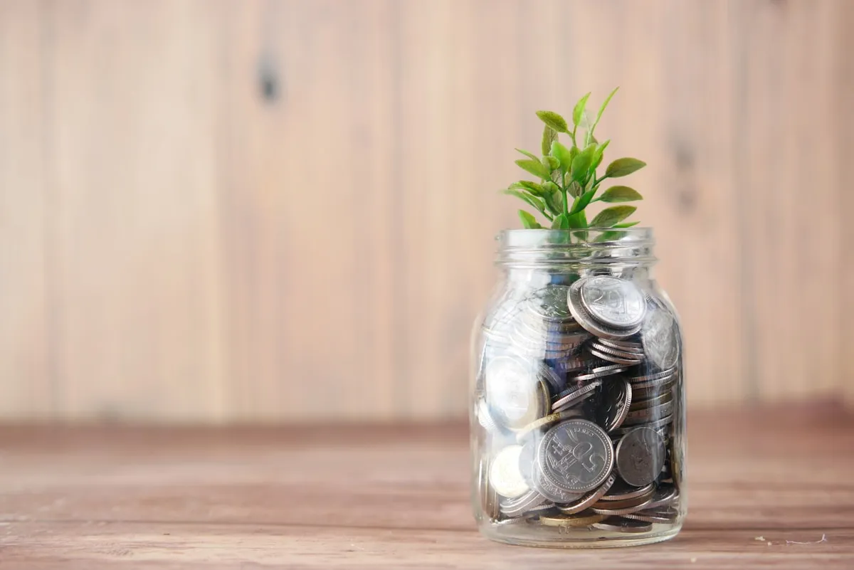 A glass jar filled with coins and a small plant growing from the top, symbolizing steady investment growth over time