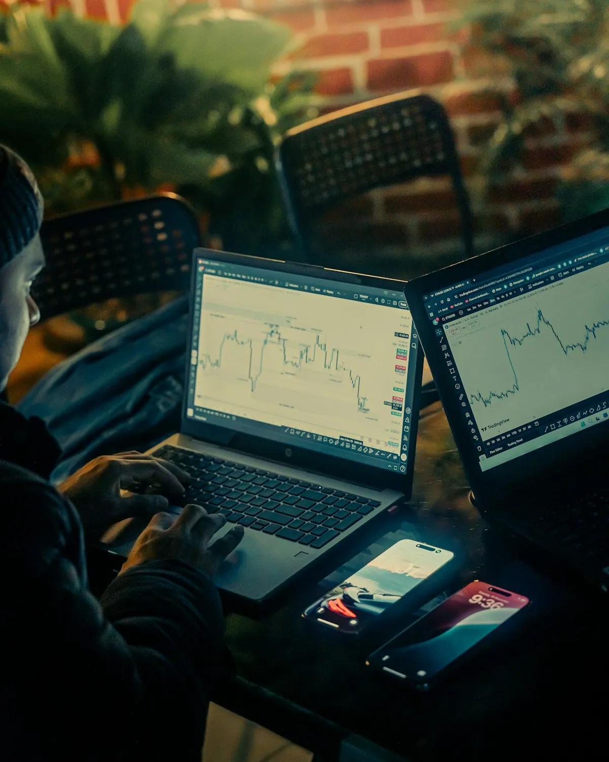Person analyzing stock charts on multiple laptop screens, representing the research needed to understand gold pricing